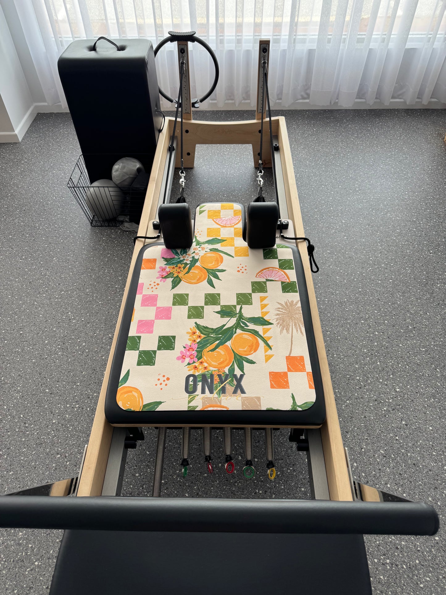 A rectangular Pilates reformer mat with a colorful floral and citrus fruit pattern, featuring the brand name 'ONYX' on the bottom right corner.