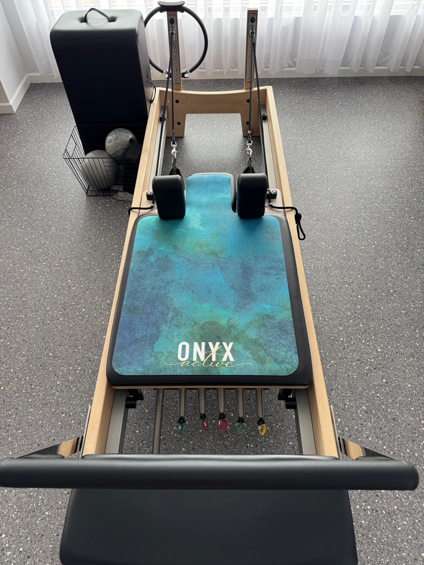 A green and blue watercolor design reformer mat with the brand 'ONYX' visible.